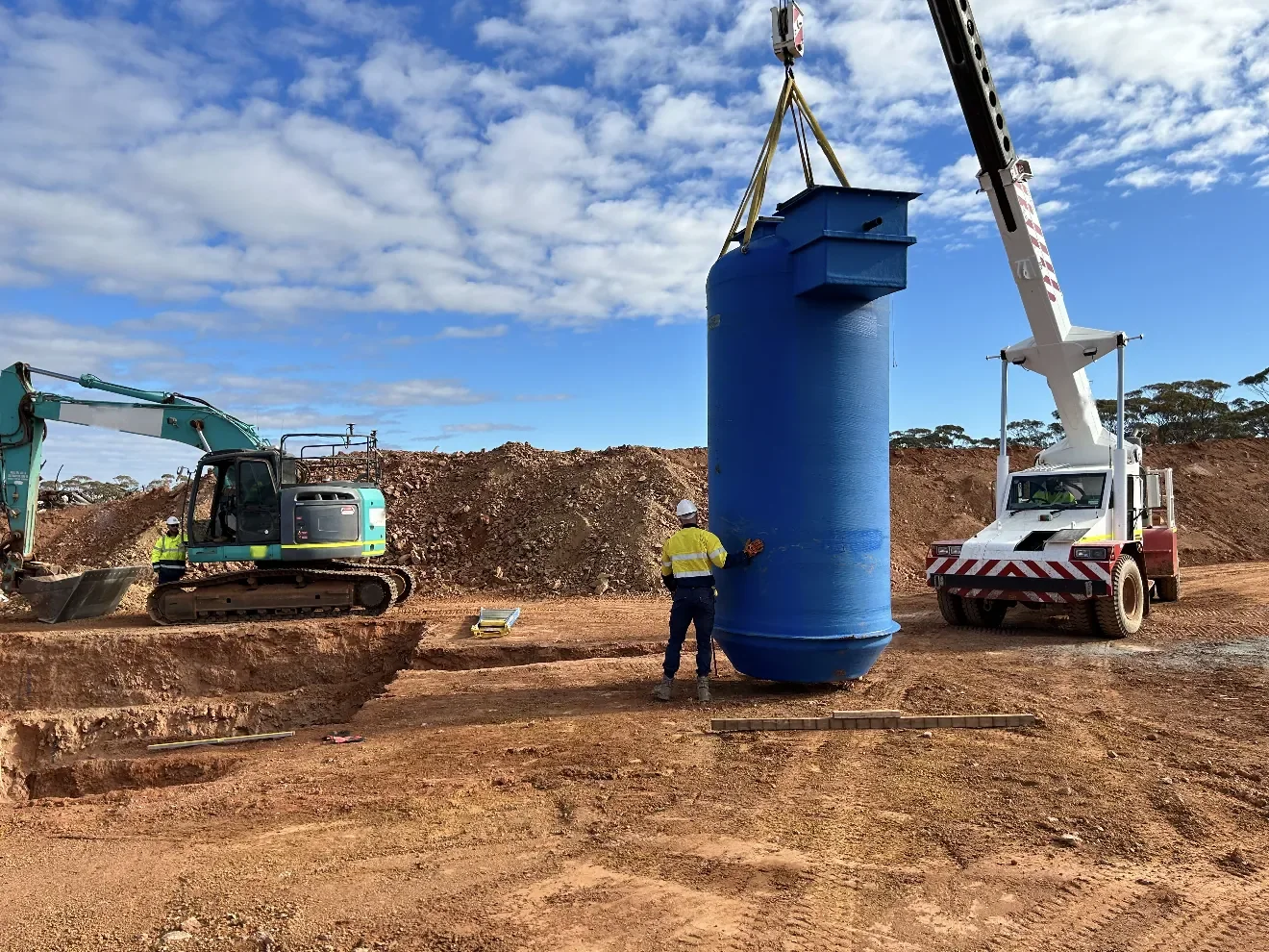 A worker in high-visibility clothing guiding a tank as it is lifted by crane